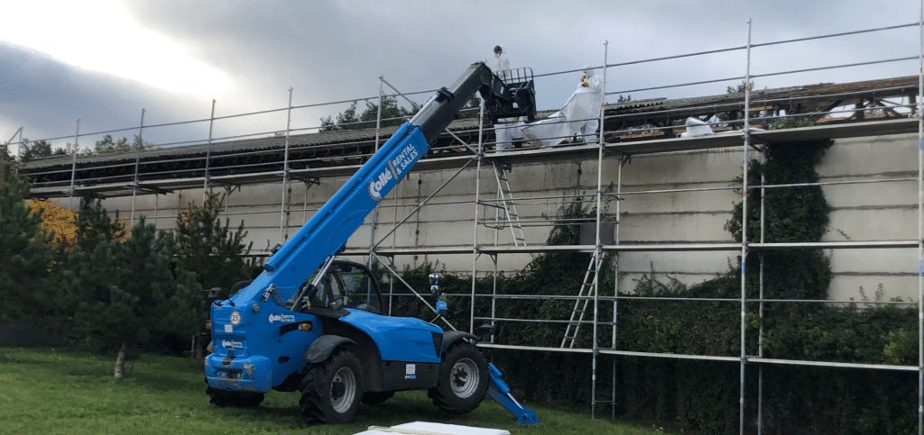 Telehandler mit blauem Ausleger auf Baustelle mit Stahlgerüst und Trapezblech-Dacheindeckung
