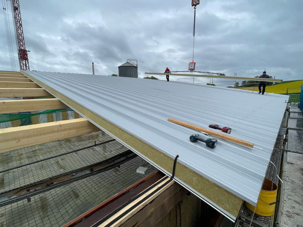 Dachneueindeckung mit Trapezblech: Montage von silbernem Trapezblech und Wärmedämmung auf großflächigem Gewerbeflachdach, Handwerker bei Installation