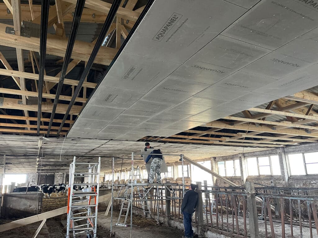 Dachdämmung und Deckenverkleidung in einer landwirtschaftlichen Halle – Montage von Leichtbausystemen durch Handwerker auf Gerüst
