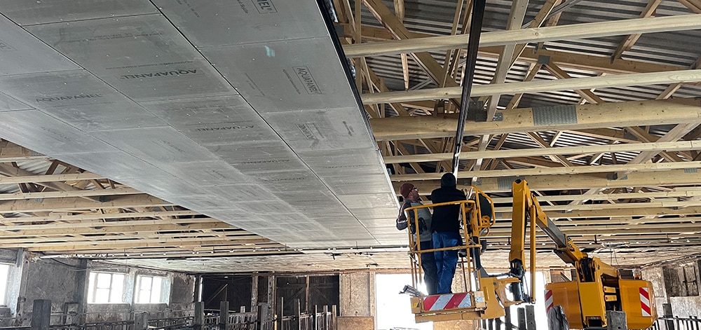 Arbeiter auf Hubarbeitsbühne montiert Trapezbleche an Decke einer gewerblichen Halle während Dachsanierung