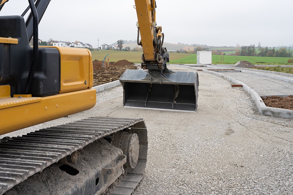 Baggerschaufel beim Erdbau auf einer Baustelle mit Kiesaufschüttung und Betonrahmen im Hintergrund