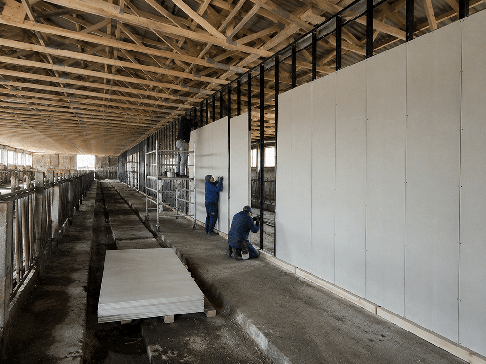 Montage von Wandsystemen in Leichtbauweise in einer landwirtschaftlichen Halle – Arbeiter installieren weiße Wandpaneele